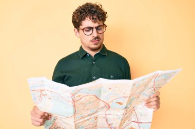 Kıvırcık saçlı, elinde şehir haritası tutan, kuşkucu ve gergin genç beyaz bir adam sorun yüzünden üzgün. negatif kişi. 