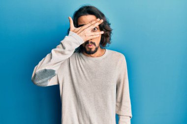Gündelik kıyafetler giyen genç İspanyol adam şok içinde yüzünü ve gözlerini eliyle kapatıyor, parmaklarından korkuyla bakıyor. 