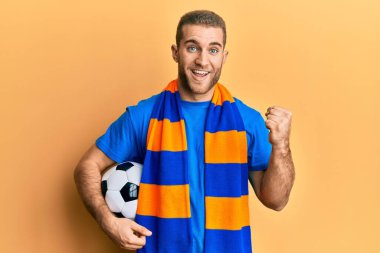 Beyazlı genç adam futbol holiganları top tutarak tezahürat yapıyor gururla haykırıyor, zaferi kutluyor ve başarıyı kollarını kaldırarak kutluyor. 