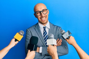 Sakallı kel bir adam mikrofonlar tutan ve kollarını kavuşturup kameraya gülümseyen gazeteciler tarafından sorgulanıyor. pozitif kişi. 