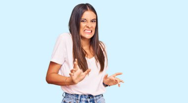 Gündelik beyaz tişört giyen genç İspanyol kadın tiksindirici bir ifade takınıyor ve tiksindirici bir yüz ifadesi takınıyor.. 