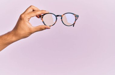 İzole edilmiş pembe arka planda gözlük tutan İspanyol bir adamın eli..