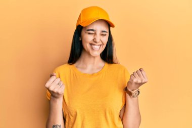 Teslimat üniforması giyen genç İspanyol kadın ve başarı için heyecanlı kolları havada ve gözleri kapalı zaferi kutlarken gülümsüyor. Kazanan konsept. 