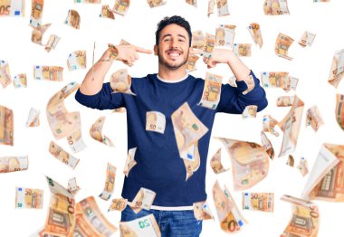 Günlük kıyafetler giyen, neşeli gülümseyen, parmaklarıyla ve ağzıyla işaret eden İspanyol genç bir adam. diş sağlığı kavramı.