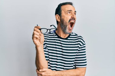 Orta yaşlı İspanyol bir adam gündelik kıyafetler giyiyor ve elinde gözlükler var kızgın ve kızgın çığlık atıyor sinirli ve öfkeli, öfkeyle bağırıyor. öfke ve agresif konsept. 
