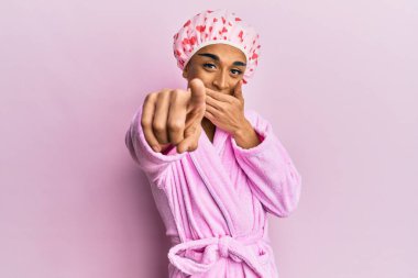 Duş havlusu şapkası ve bornoz takan İspanyol adam sana gülüyor, eli ağzında kamerayı işaret ediyor, utanç ifadesi var. 