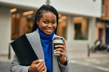 Genç Afrikalı Amerikalı iş kadını gülümseyerek şehirde kahve içiyor..