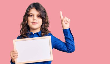 Uzun saçlı tatlı İspanyol çocuk elinde boş beyaz karatahta ile bir fikir ya da soru işareti ile şaşırdı. 