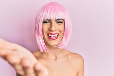 Pembe peruk takmış genç bir adam gülümseyerek selamlama ve hoş geldin demek için tokalaşıyor. başarılı iş. 