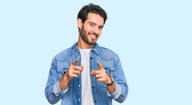 Günlük kıyafetler giyen genç İspanyol adam mutlu ve komik yüzüyle kamerayı işaret ediyor. iyi enerji ve titreşimler. 