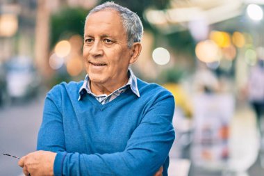 Yaşlı, gri saçlı, kollarını kavuşturmuş, gülümseyen, mutlu bir adam..