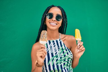 Genç Afrikalı Amerikalı kadın gülümseyerek şehirde dondurma yiyor..