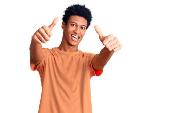 Genç Afro-Amerikan adam günlük giysiler giyip olumlu jestler yapıyor. Elleriyle gülümsüyor ve başarı için seviniyor. kazanan jest. 