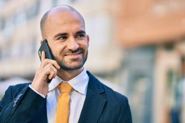 Genç Latin kökenli kel iş adamı gülümsüyor. Şehirdeki akıllı telefondan mutlu bir şekilde konuşuyor..