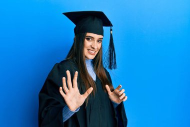 Mezuniyet şapkası ve tören cübbesi giymiş güzel esmer bir kadın tiksindirici ve tiksindirici bir ifade takınıyor çünkü tiksinti tepki veriyor. Eller havada. 