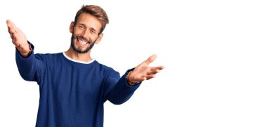 Sakallı, sıradan bir süveter giyen yakışıklı sarışın kameraya sarılıp gülümsüyor. Mutluluğu kucaklayan neşeli bir ifade.. 