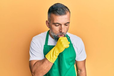 Orta yaşlı, daha temiz önlük ve eldiven giyen yakışıklı bir adam kendini kötü hissediyor ve soğuk algınlığı veya bronşitin belirtisi olarak öksürüyor. sağlık hizmeti kavramı. 