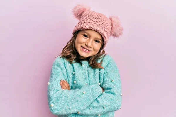 ウールのセーターとかわいい冬の帽子の幸せな顔を身に着けている小さな美しい女の子は カメラを見て交差腕で笑顔 正の人 — ストック写真