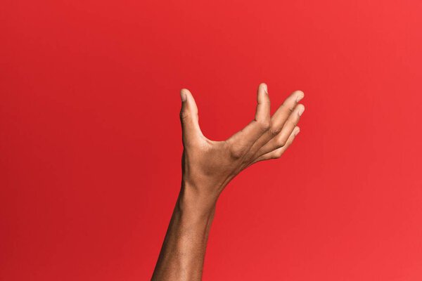 Hand of hispanic man over red isolated background picking and taking invisible thing, holding object with fingers showing space 