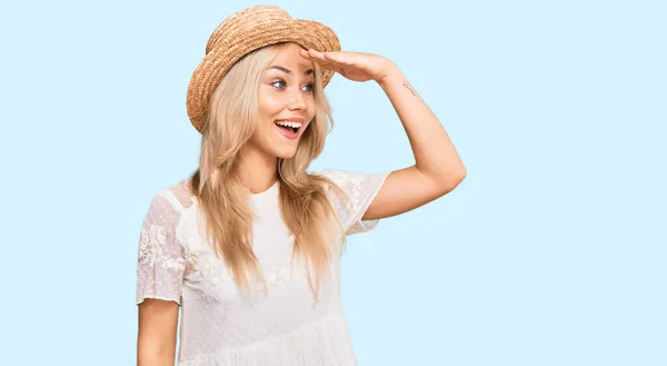 若いブロンドの女の子は夏の帽子をかぶって非常に満足し 遠くを見て笑顔頭の上に手で 検索の概念 — ストック写真