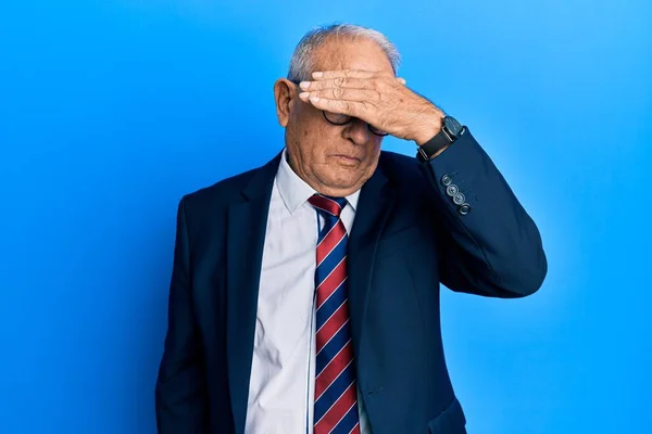 Senior caucasian man wearing business suit and tie covering eyes with hand, looking serious and sad. sightless, hiding and rejection concept