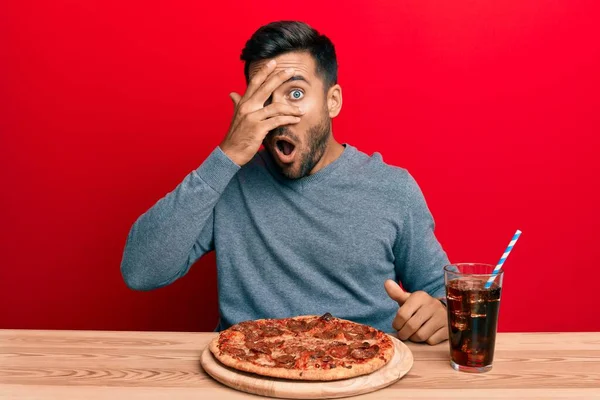 ハンサムなヒスパニック系の男食べるおいしいペパロニピザのピーキングでショックカバー顔と目で手で 指を通して恐れて見て — ストック写真