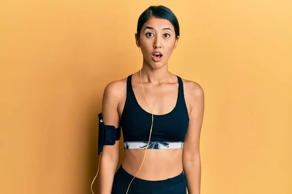 Beautiful asian young sport woman wearing sportswear and earphones scared and amazed with open mouth for surprise, disbelief face