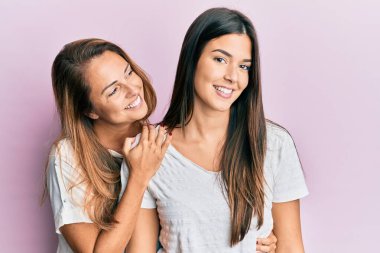 Güzel İspanyol anne ve kızı gülümsüyor. Mutlu bir şekilde pembe arka planda sarılıyorlar..