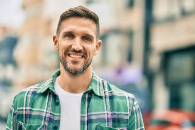 Genç beyaz adam gülümseyerek şehirde mutlu mesut duruyor..