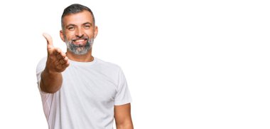 Orta yaşlı, beyaz tişört giyen yakışıklı bir adam dostça gülümseyerek selamlama ve hoş geldin diyor. başarılı iş. 