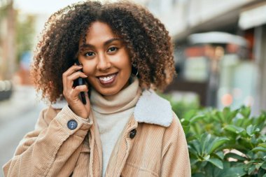 Genç Afrikalı Amerikalı kadın gülümsüyor. Şehirdeki akıllı telefondan mutlu bir şekilde konuşuyor..