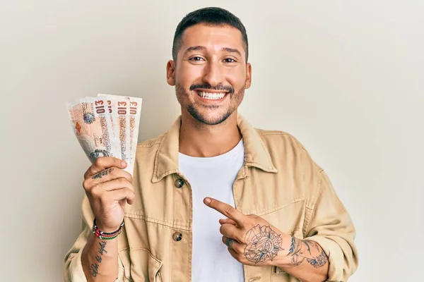 英俊的男人 身上有纹身 手里拿着10英镑的英国钞票 脸上挂着幸福的笑容 手指手画脚 — 图库照片