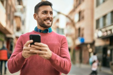Genç İspanyol adam şehirde akıllı telefon kullanarak mutlu gülümsüyor..