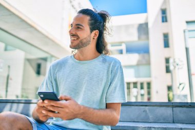 Genç İspanyol adam şehirde akıllı telefon kullanarak mutlu gülümsüyor..