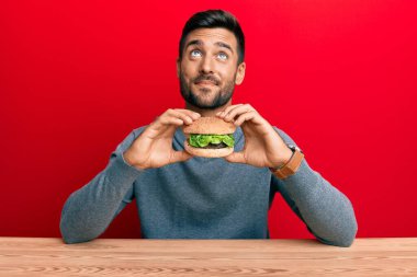 Yakışıklı İspanyol bir adam lezzetli bir klasik burger yiyor. Gülümsüyor, yan tarafa bakıyor ve düşünüyor.. 
