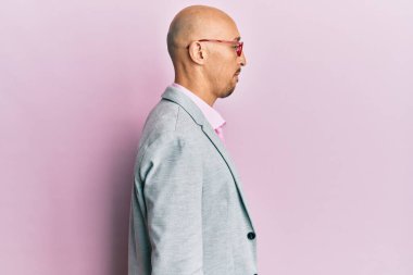 Sakallı, iş elbiseleri ve gözlüklü kel bir adam yan tarafa bakıyor, rahat poz veriyor, kendine güvenen bir gülümsemesi var.. 