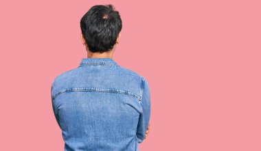 Gündelik kıyafetler giyen genç İspanyol adam arkasını dönüp kollarını kavuşturarak başka tarafa bakıyor. 