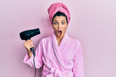 Duşta bornoz giyen genç İspanyol kadın kurutucu kullanıyor korkmuş ve ağzı açık şaşırmış, inançsız yüz. 