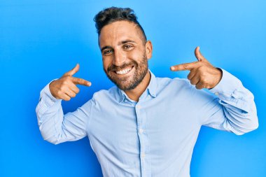 Sakallı, sıradan kıyafetler giyen, neşeli gülümseyen, parmaklarıyla ve ağzıyla işaret eden yakışıklı bir adam. diş sağlığı kavramı. 