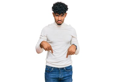 Gündelik kazak giyen genç Arap adam üzgün ve üzgün görünüyor, parmaklarıyla yön gösteriyor, mutsuz ve depresif.. 