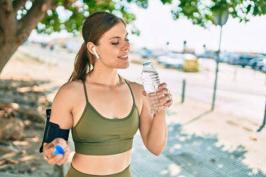 Genç sarışın sporcu şehirde bir şişe su içerek egzersiz yapıyor..