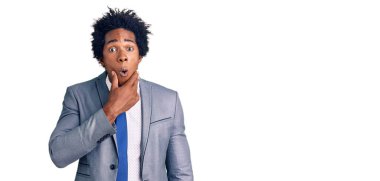 Handsome african american man with afro hair wearing business jacket looking fascinated with disbelief, surprise and amazed expression with hands on chin 