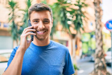 Genç beyaz adam gülümsüyor. Şehirdeki akıllı telefondan konuşuyor..
