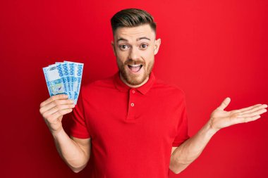 Genç kızıl saçlı adam elinde 1000 Macar banknotuyla başarıyı mutlu bir gülümsemeyle kutluyor ve kazanan el kaldırarak ifade ediyor. 