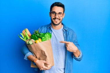 Ekmek ve bakkaliyeyle dolu kağıt poşet tutan genç İspanyol adam mutlu bir şekilde elini ve parmağını gösterdi. 