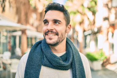 Şehre yürürken atkı takan, mutlu gülümseyen genç İspanyol adam..