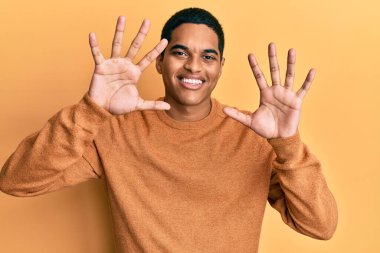 Genç, yakışıklı, sıradan bir süveter giyen, on numarayı gösteren, kendinden emin ve mutlu gülümseyen İspanyol bir adam.. 