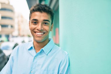 Genç Latin adam gülümsüyor. Şehrin duvarına yaslanmış mutlu bir şekilde..