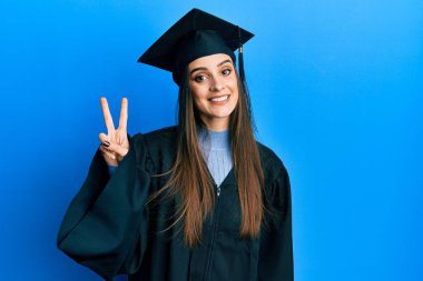 Mezuniyet şapkası ve tören cübbesi giyen güzel esmer bir kadın iki numaralı parmaklarıyla kendini beğenmiş ve mutlu gülümserken onu gösteriyor.. 