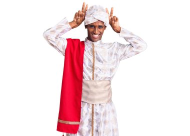 Geleneksel Sherwani sari elbiseleri giyen Afrikalı yakışıklı adam komik ve deli pozu veriyor parmakları tavşan kulağı gibi, neşeli gülümsüyor. 